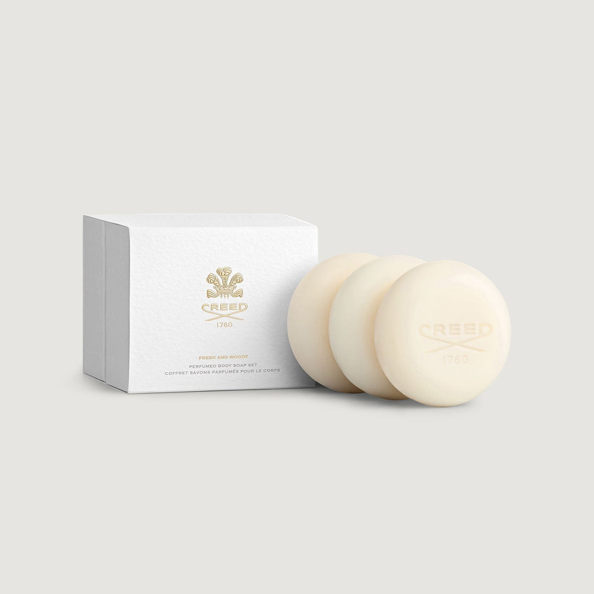 Two cream-colored soaps with a white box featuring the Creed logo on a light gray background.